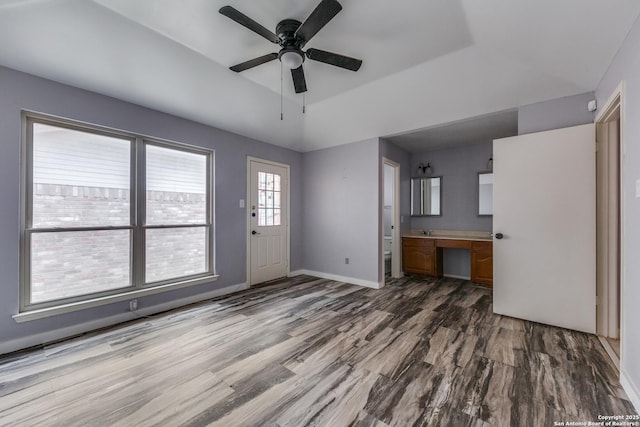 unfurnished living room with built in desk, a raised ceiling, ceiling fan, and wood-type flooring