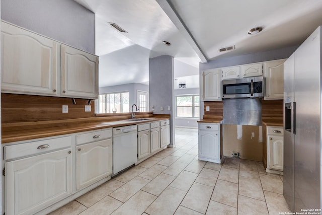 kitchen with white cabinets, appliances with stainless steel finishes, lofted ceiling with beams, and tasteful backsplash