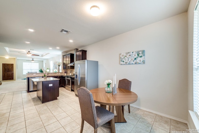 dining area with ceiling fan, a raised ceiling, and light tile patterned floors