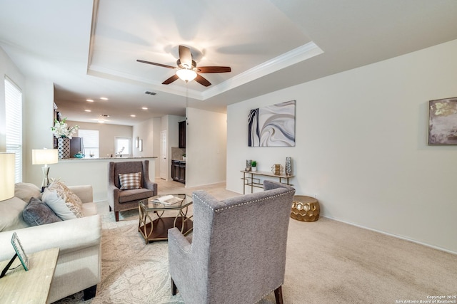 carpeted living room featuring ceiling fan, a tray ceiling, and ornamental molding