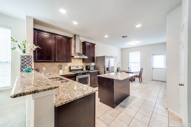 kitchen featuring appliances with stainless steel finishes, a center island, wall chimney range hood, sink, and kitchen peninsula