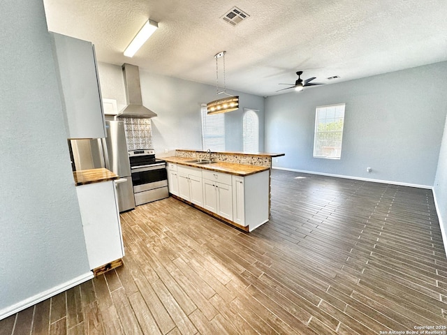 kitchen with white cabinetry, appliances with stainless steel finishes, butcher block countertops, and wall chimney exhaust hood