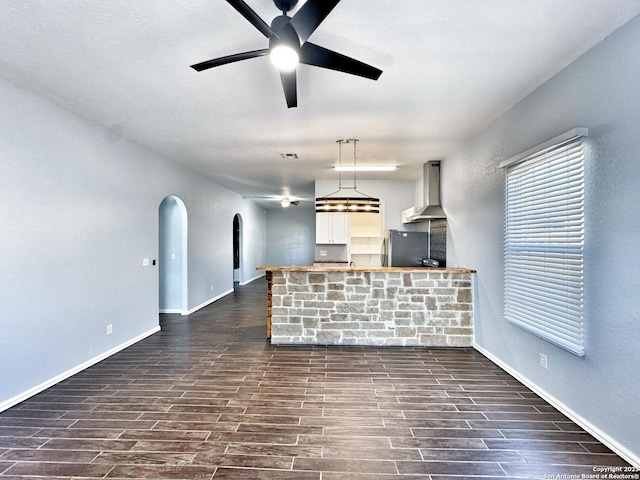 kitchen featuring ceiling fan, wall chimney exhaust hood, dark wood-type flooring, white cabinetry, and stainless steel refrigerator