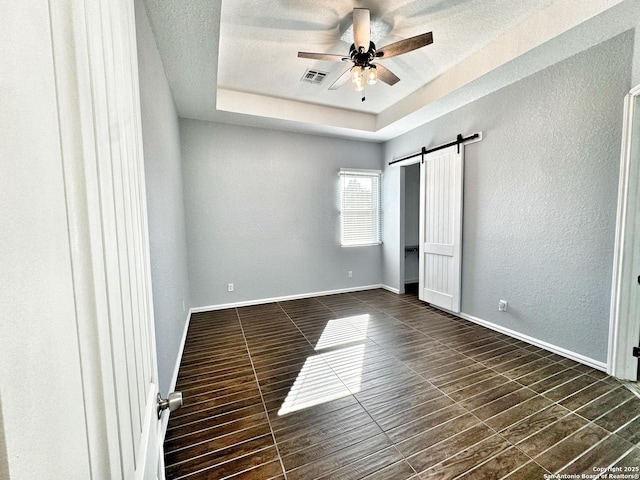 unfurnished bedroom with ceiling fan, a tray ceiling, and a barn door