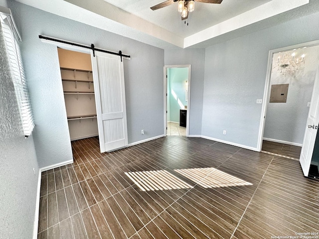 unfurnished bedroom with ceiling fan, a barn door, a walk in closet, connected bathroom, and a closet