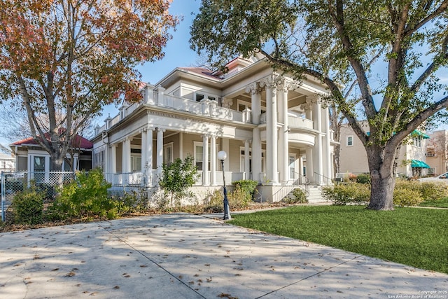 greek revival house with a balcony, a porch, and a front lawn