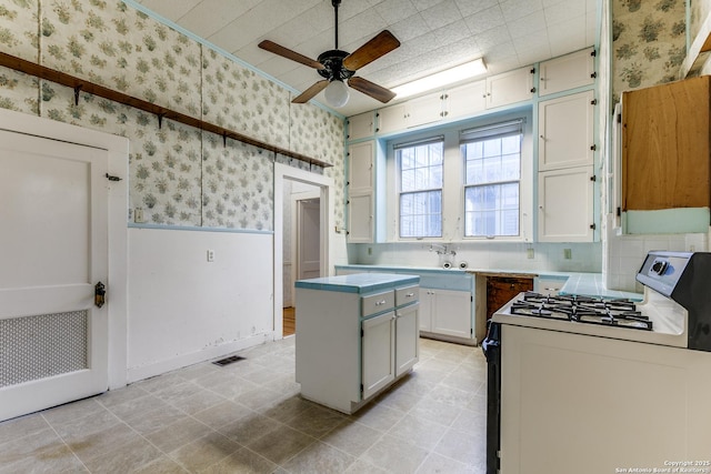 kitchen featuring white cabinets, a center island, range with gas stovetop, tasteful backsplash, and ceiling fan