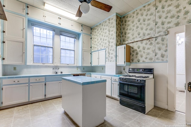 kitchen with ceiling fan, gas range oven, white cabinets, a kitchen island, and tile counters