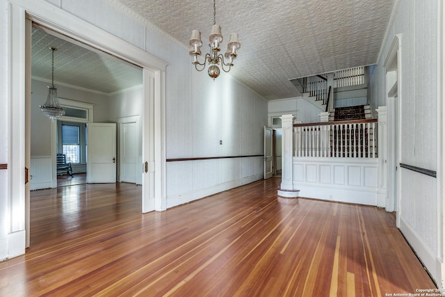 empty room with wood-type flooring, crown molding, and a notable chandelier