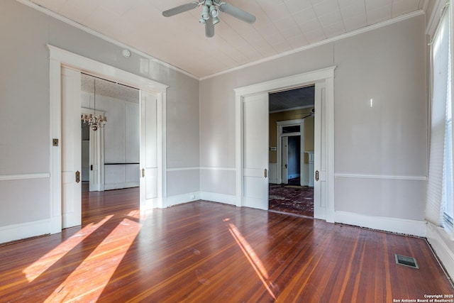 empty room with ceiling fan with notable chandelier, dark hardwood / wood-style flooring, and ornamental molding