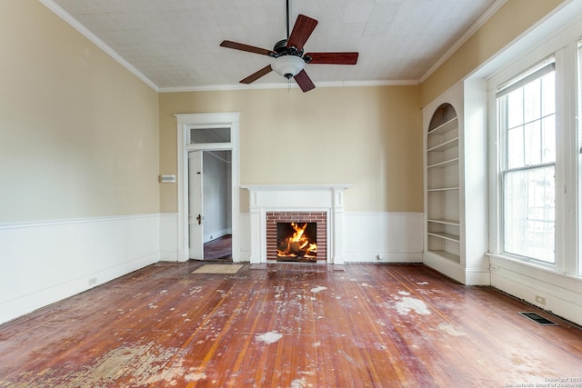 unfurnished living room featuring wood-type flooring, ceiling fan, built in shelves, a fireplace, and ornamental molding