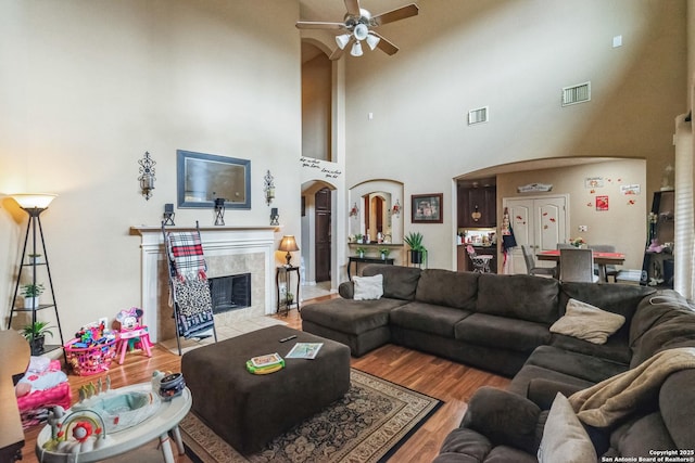 living room featuring a high ceiling, a tiled fireplace, ceiling fan, and light hardwood / wood-style floors