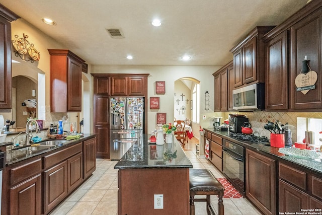 kitchen with sink, light tile patterned floors, appliances with stainless steel finishes, a kitchen breakfast bar, and a center island