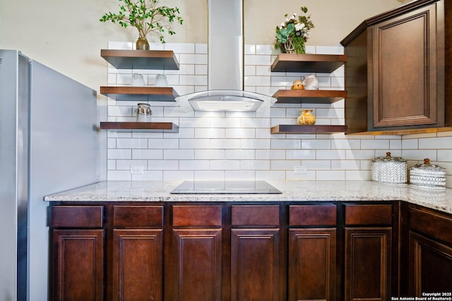 kitchen featuring black electric stovetop, wall chimney range hood, light stone countertops, and stainless steel fridge