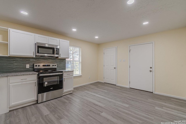 kitchen featuring light stone countertops, appliances with stainless steel finishes, white cabinets, light wood-type flooring, and backsplash