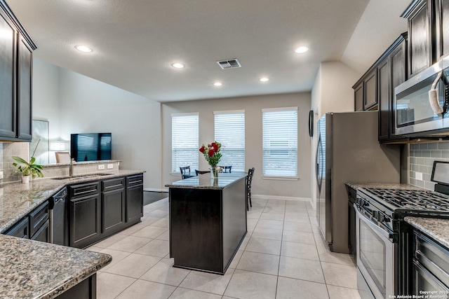 kitchen with light stone counters, backsplash, a center island, and appliances with stainless steel finishes