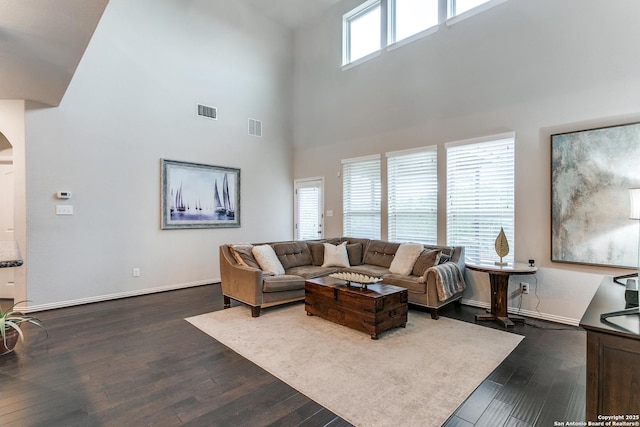 living room with dark wood-type flooring, plenty of natural light, and a towering ceiling