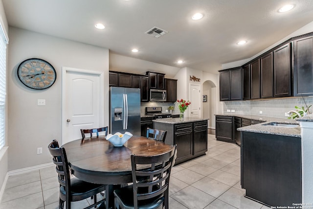 kitchen with a center island, light stone countertops, sink, stainless steel appliances, and light tile patterned flooring