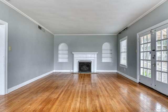 unfurnished living room with built in shelves, french doors, light wood-type flooring, a brick fireplace, and crown molding