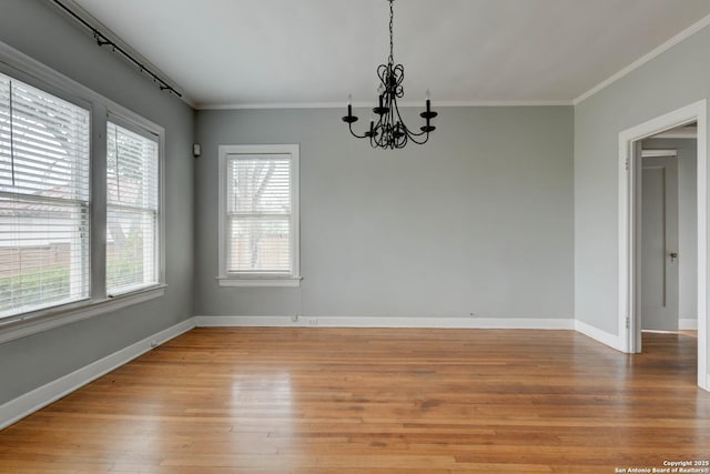 spare room with light hardwood / wood-style floors, a notable chandelier, a wealth of natural light, and ornamental molding