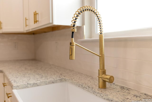 interior details with white cabinets, light stone countertops, and sink