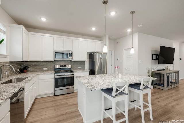 kitchen featuring hanging light fixtures, sink, a kitchen island, white cabinets, and stainless steel appliances