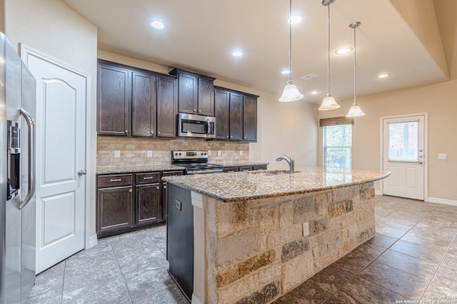 kitchen with pendant lighting, appliances with stainless steel finishes, sink, a kitchen island with sink, and light stone counters