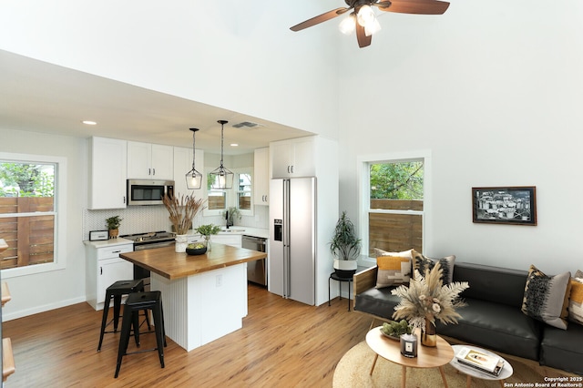 kitchen featuring butcher block counters, appliances with stainless steel finishes, white cabinetry, a kitchen island, and pendant lighting