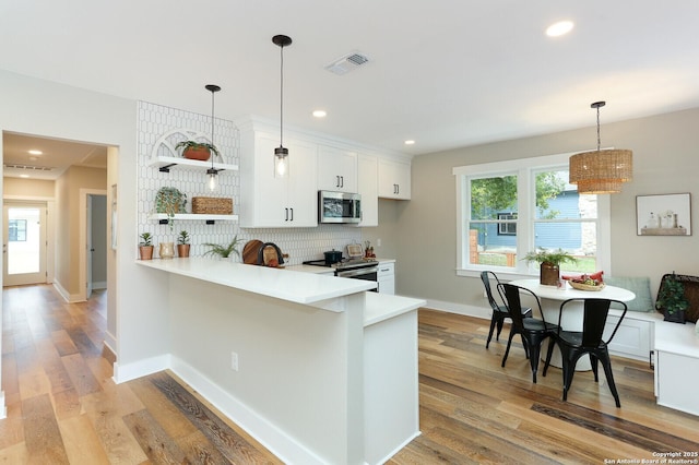 kitchen with pendant lighting, white cabinets, appliances with stainless steel finishes, decorative backsplash, and kitchen peninsula