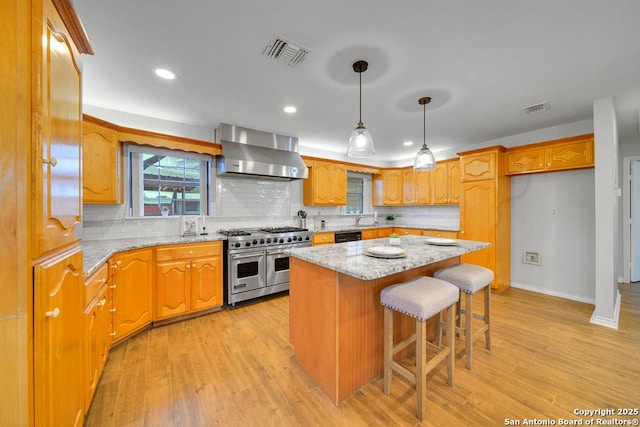 kitchen featuring a center island, light stone countertops, wall chimney range hood, backsplash, and range with two ovens