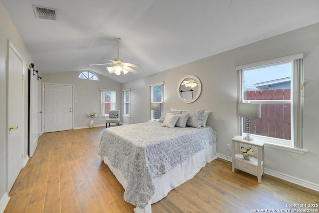 bedroom featuring ceiling fan, a barn door, multiple windows, and hardwood / wood-style flooring