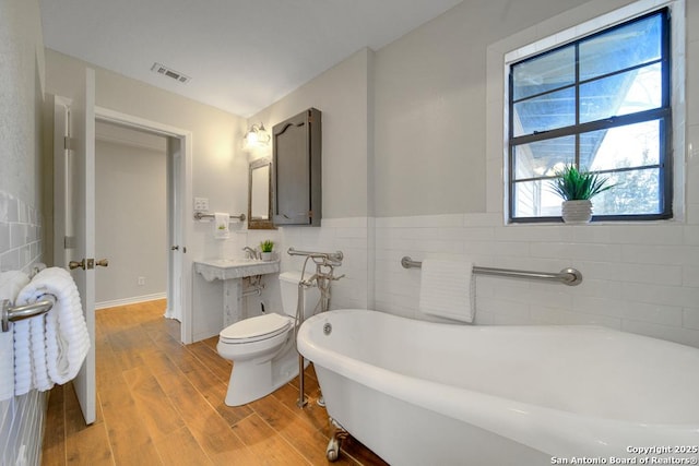 bathroom with tile walls, toilet, and a bath