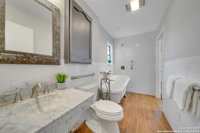 bathroom with hardwood / wood-style flooring, toilet, a tub to relax in, and tile walls