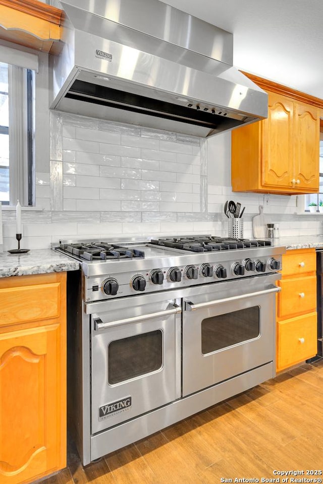 kitchen featuring exhaust hood, double oven range, light stone countertops, and tasteful backsplash