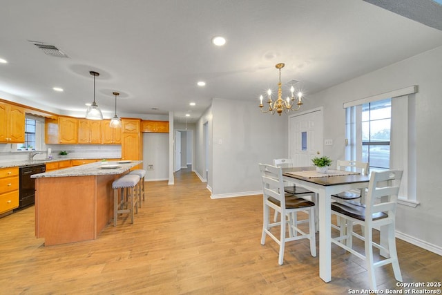 kitchen with light stone countertops, dishwasher, decorative backsplash, a kitchen island, and decorative light fixtures