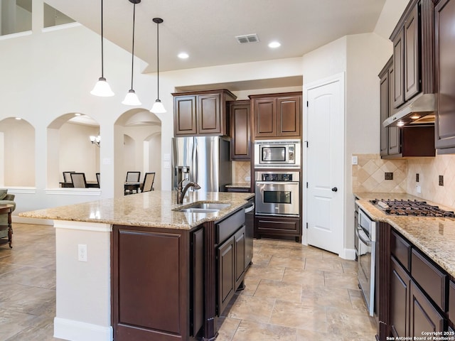 kitchen featuring pendant lighting, sink, appliances with stainless steel finishes, a kitchen island with sink, and dark brown cabinetry