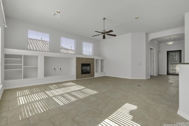 unfurnished living room with built in shelves, ceiling fan, and a tiled fireplace