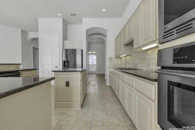 kitchen with cream cabinetry, tasteful backsplash, dark stone counters, a center island, and stainless steel appliances