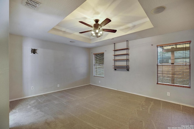 empty room with ceiling fan, carpet flooring, ornamental molding, and a tray ceiling