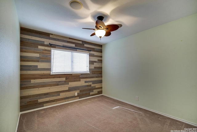 carpeted empty room featuring wooden walls and ceiling fan