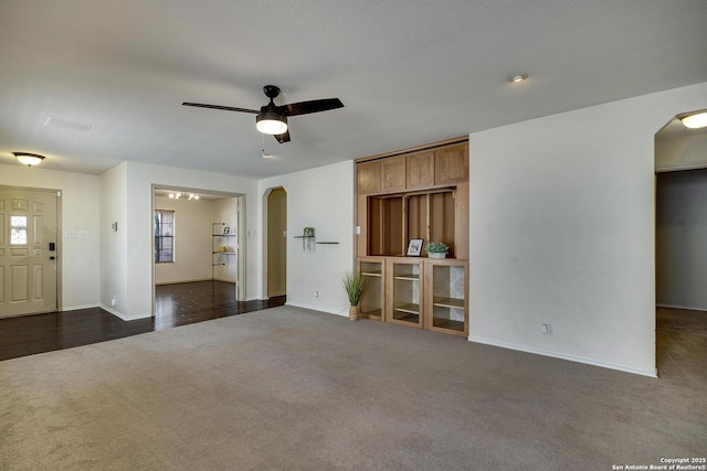 unfurnished living room featuring ceiling fan and dark colored carpet