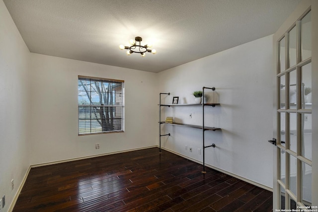 spare room with a notable chandelier, a textured ceiling, and dark hardwood / wood-style flooring