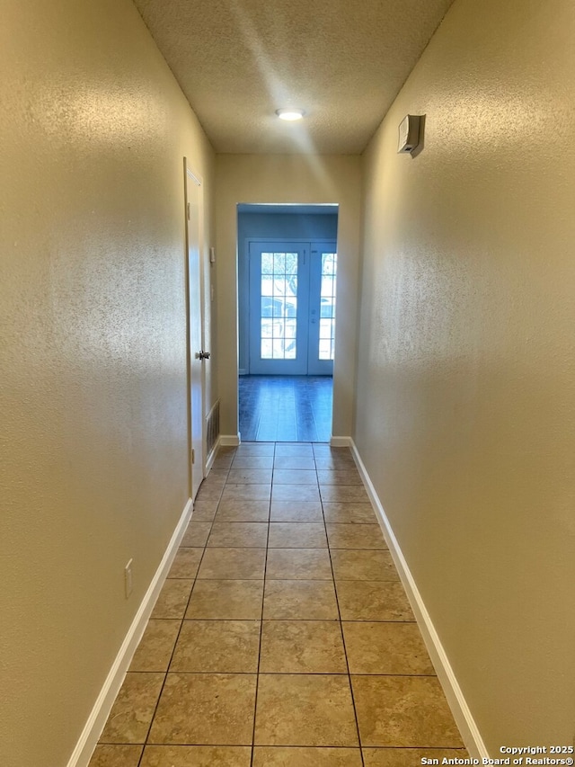 hallway with a textured ceiling and tile patterned floors