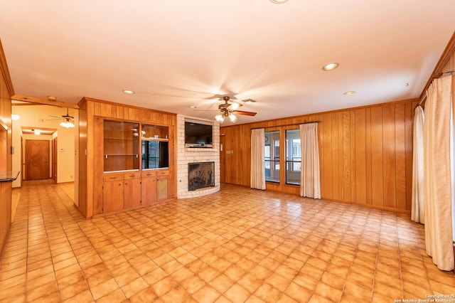 unfurnished living room featuring crown molding, a brick fireplace, wooden walls, built in features, and ceiling fan