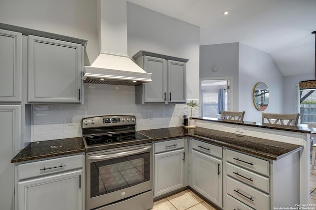 kitchen with plenty of natural light, custom exhaust hood, stainless steel range with electric cooktop, kitchen peninsula, and dark stone counters