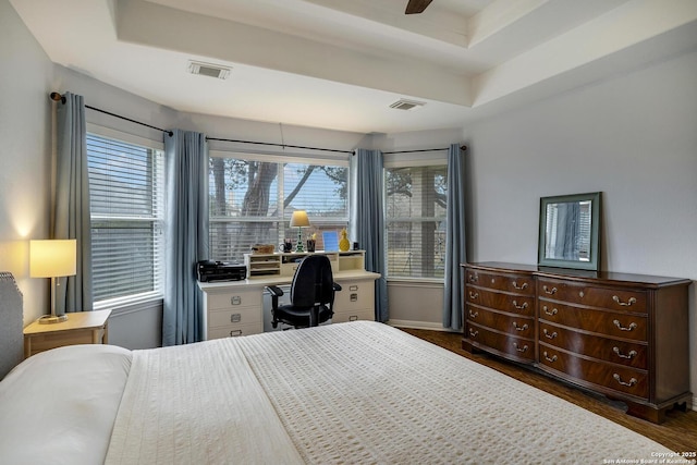 bedroom with multiple windows, dark wood-type flooring, a raised ceiling, and ceiling fan