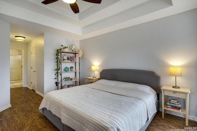 bedroom with a tray ceiling, dark wood-type flooring, ceiling fan, and ensuite bathroom