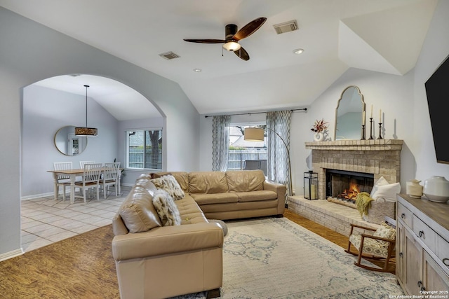 tiled living room with vaulted ceiling, ceiling fan, and a fireplace