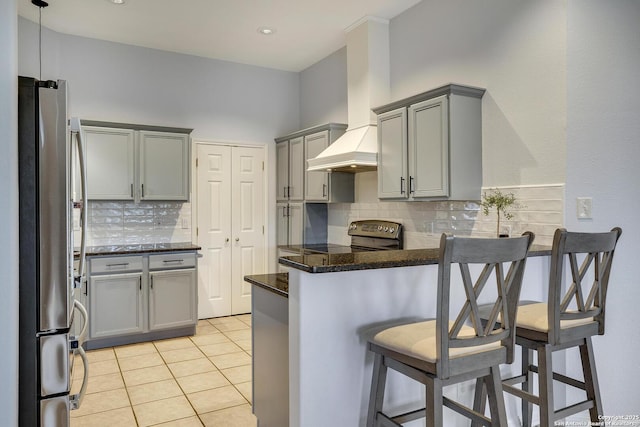 kitchen featuring a kitchen bar, range with electric stovetop, stainless steel fridge, kitchen peninsula, and custom range hood