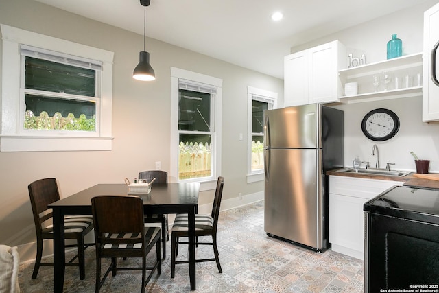 kitchen with decorative light fixtures, white cabinetry, sink, stainless steel fridge, and range with electric stovetop